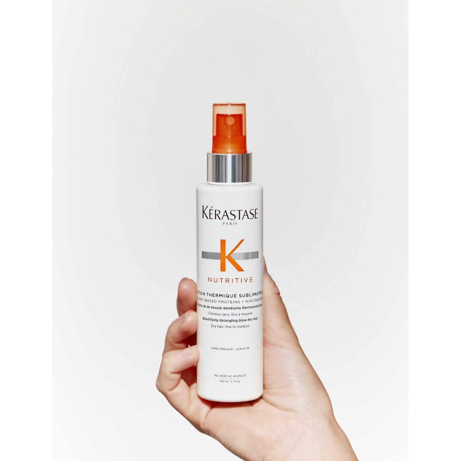 Hand holding Kérastase Nutritive Lotion Thermique Sublimatrice, a detangling blow-dry mist for dry, fine to medium hair.