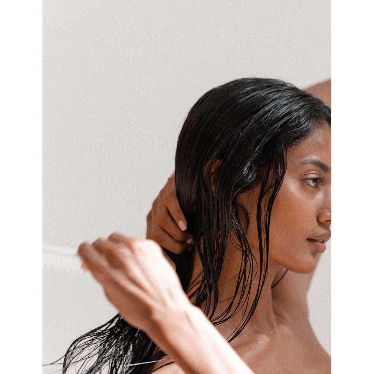 Person combing through wet hair using a fine-toothed comb, promoting healthy and nourished hair care routine.