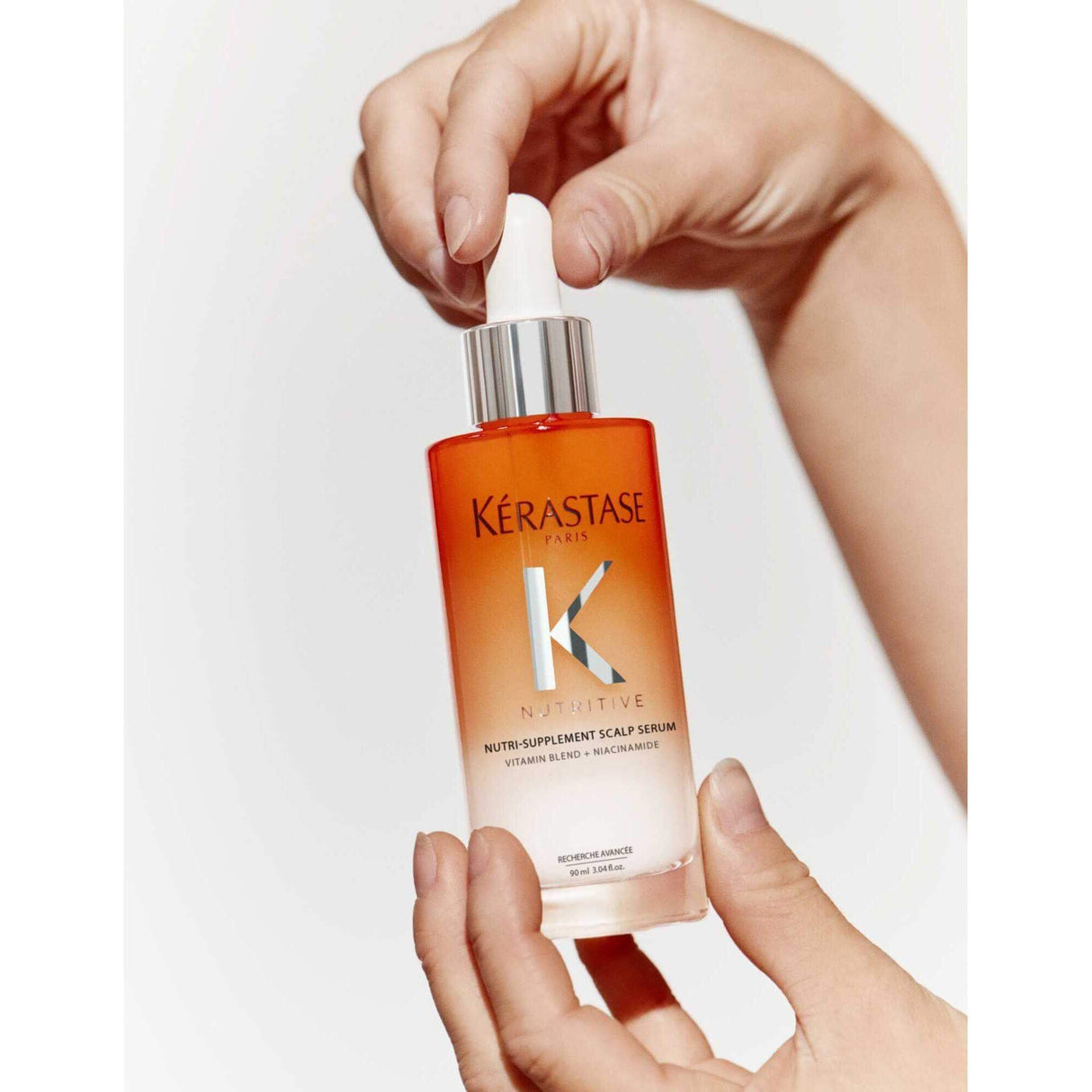 Hands holding Kérastase Nutritive Nutri-Supplement Scalp Serum with dropper bottle.