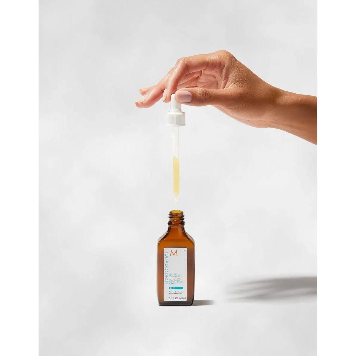 Hand holding dropper for Moroccanoil Oil-No-More Scalp Treatment bottle, effective for oily scalp with ginger oil and purifying agents.