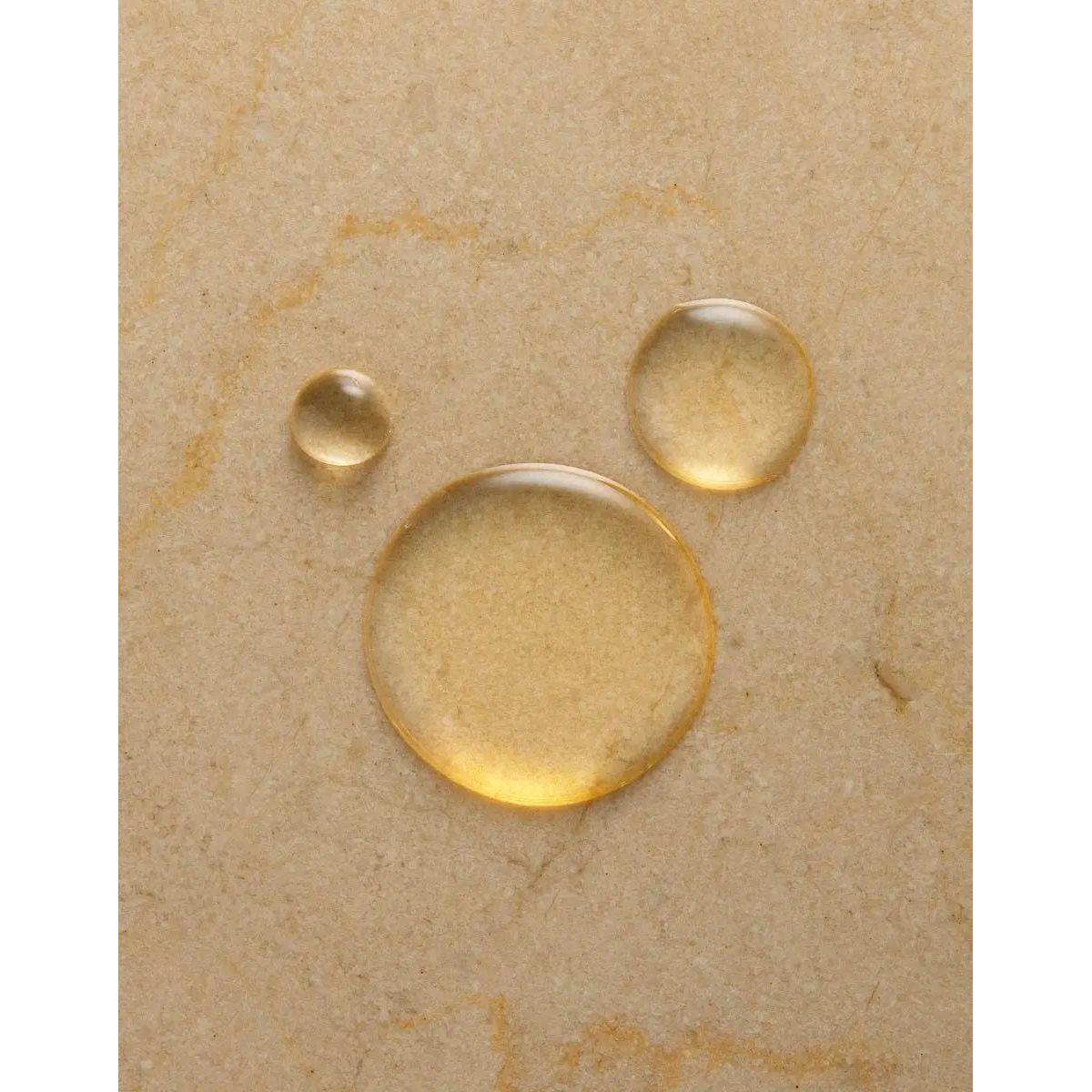 Close-up of three drops of argan oil on a stone surface, showcasing the hydrating ingredient in Original Scented Shower Gel.