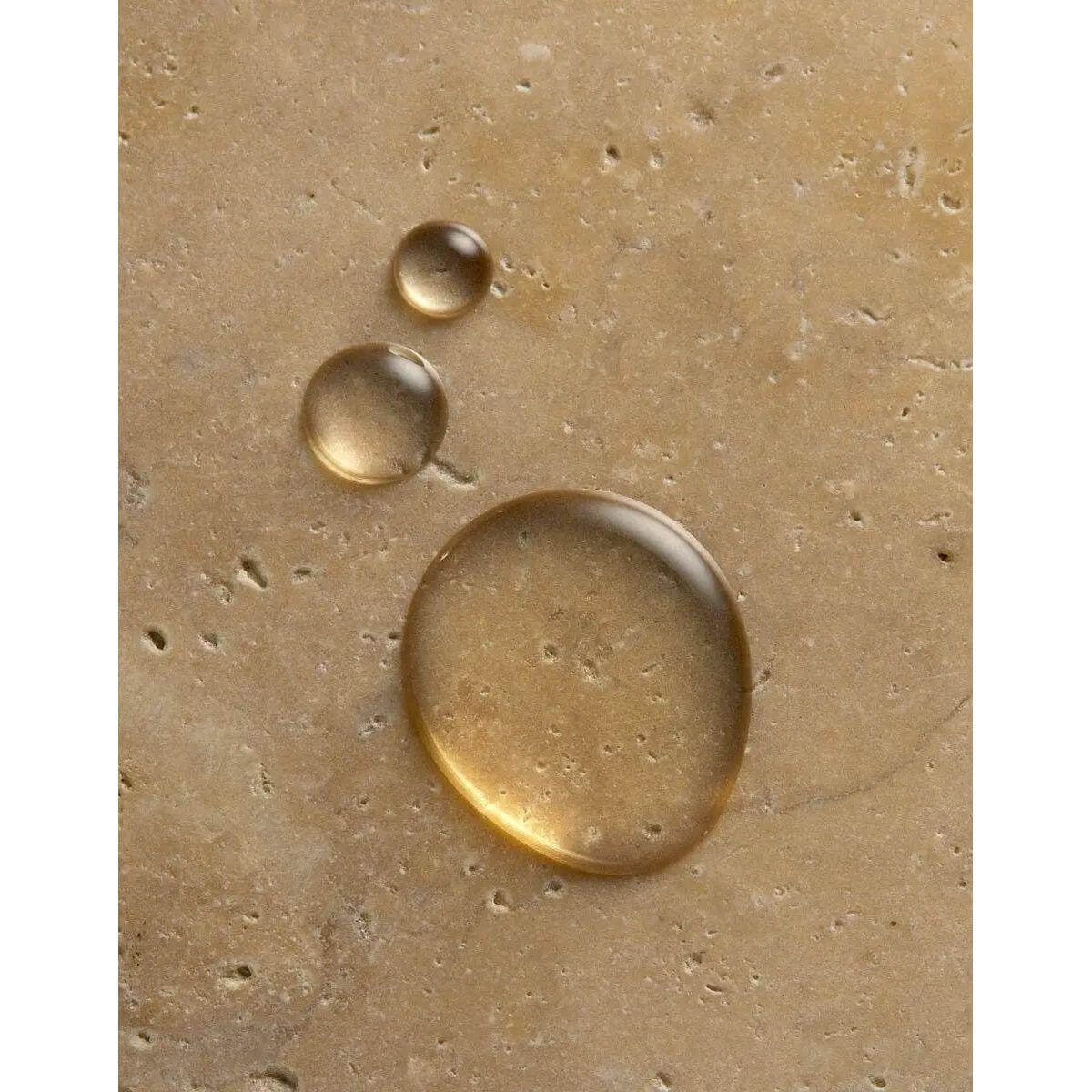 Close-up of golden liquid drops on a textured surface, representing the nourishing hydrating properties of Originale Fragrance Hand Wash.