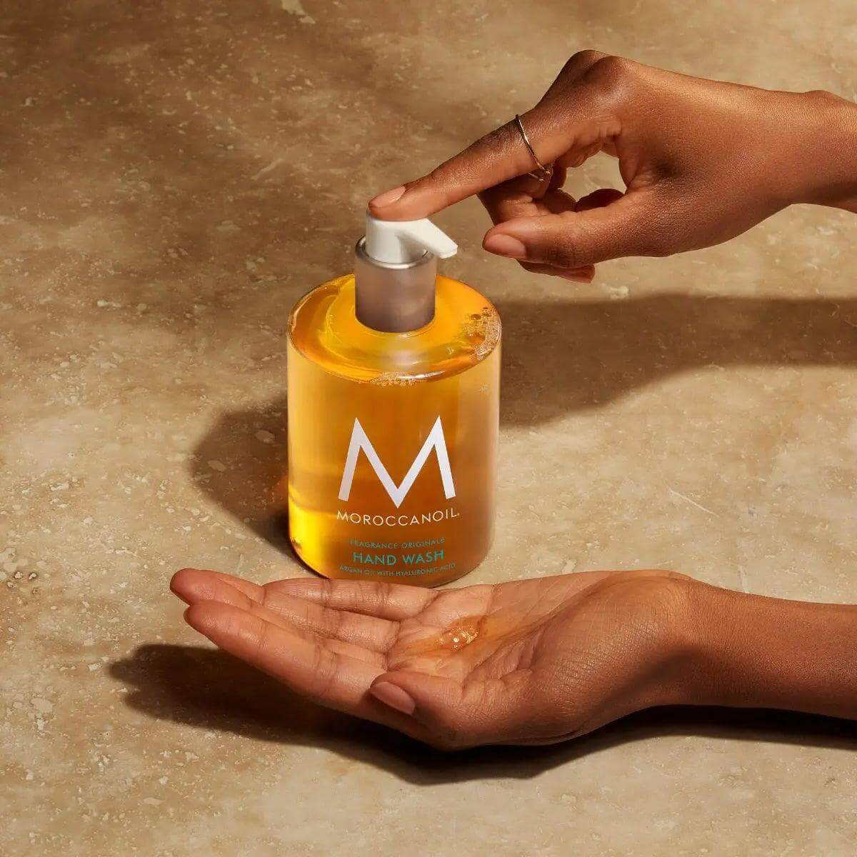 Person using Moroccanoil Originale Fragrance Hand Wash enriched with argan oil and hyaluronic acid on a countertop.