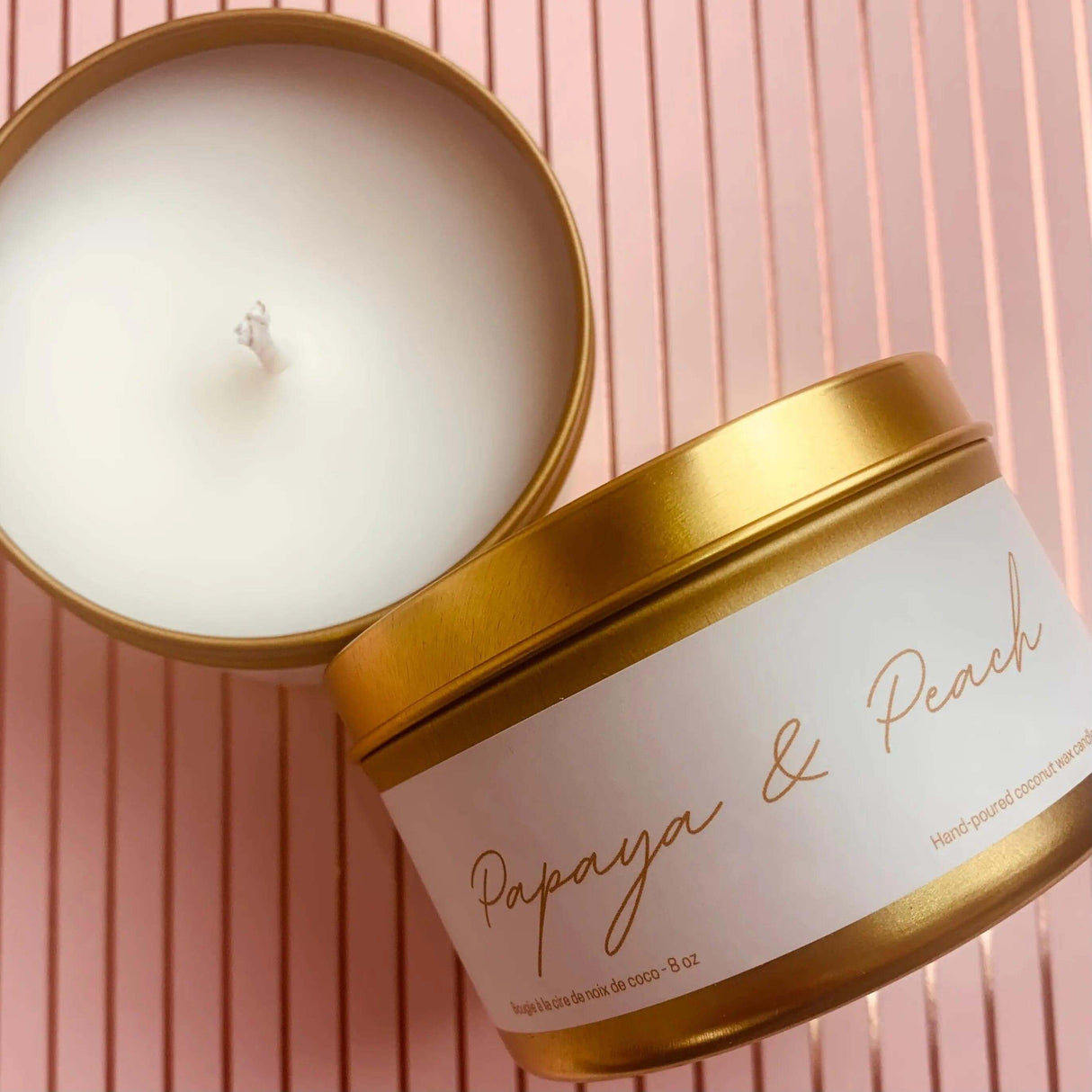 Papaya & Peach scented candle in gold tin with lid off on pink striped background, made with GMO-free coconut wax and essential oils.