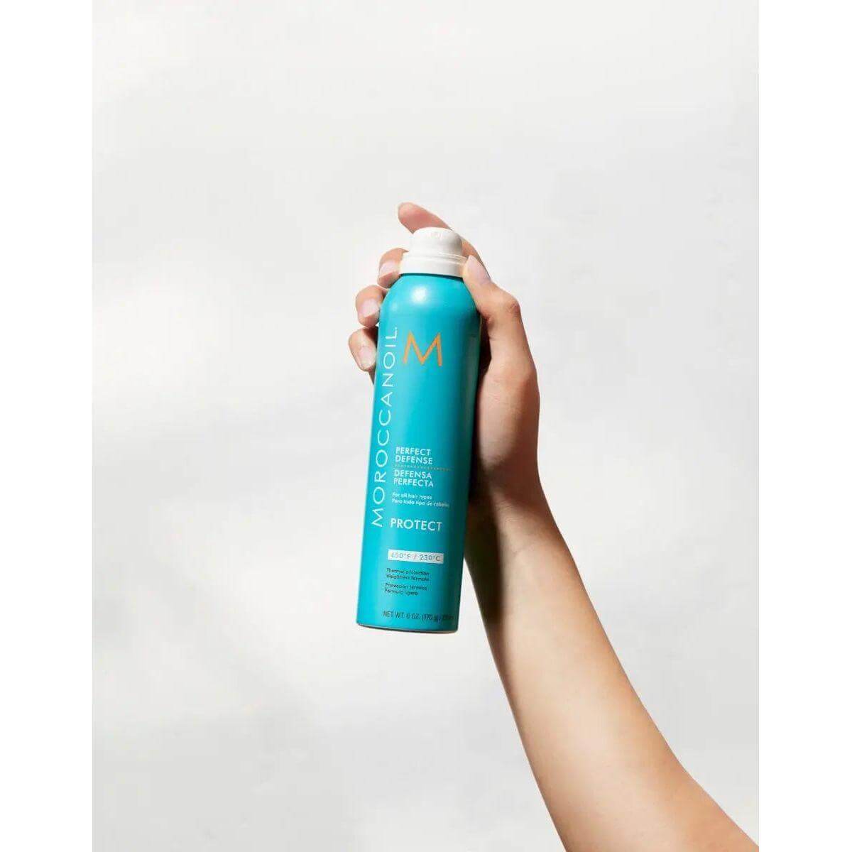 Hand holding Perfect Defense Heat Protectant spray with argan oil for hair protection.