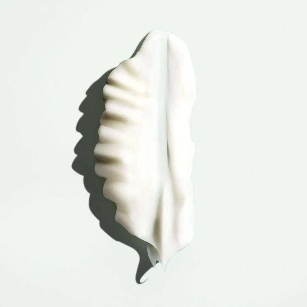Leaf-shaped dollop of Priming Lotion Leave-In Conditioning Detangler on light green background.