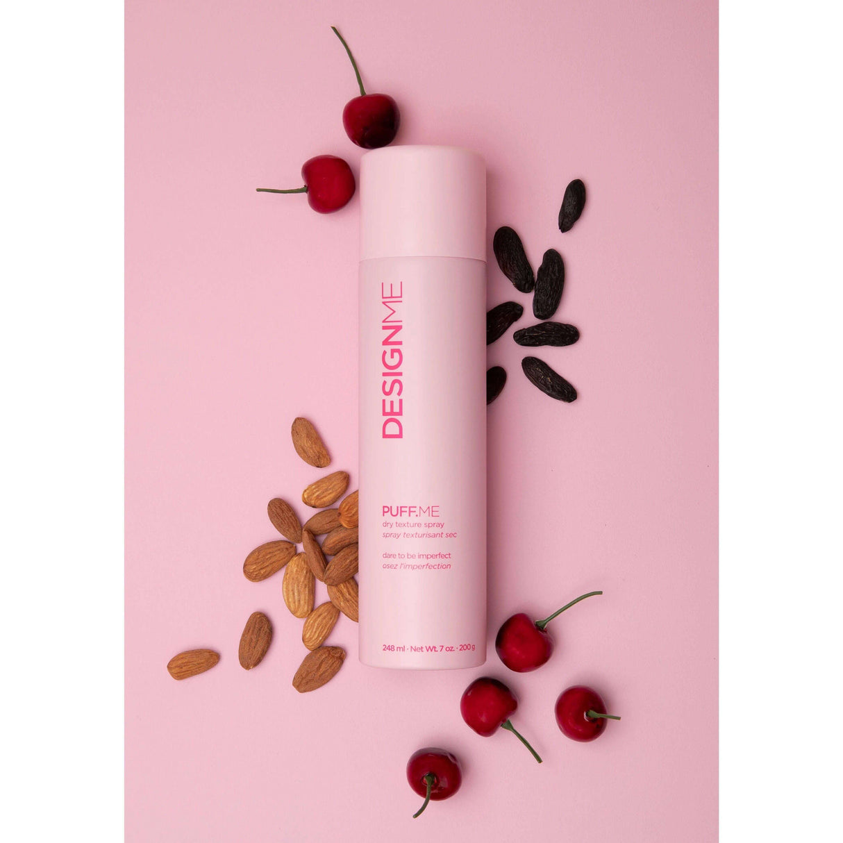 Puff.Me Dry Texture Spray by Design.Me on a pink background with almonds and cherries, offering instant volume and flexible hold.