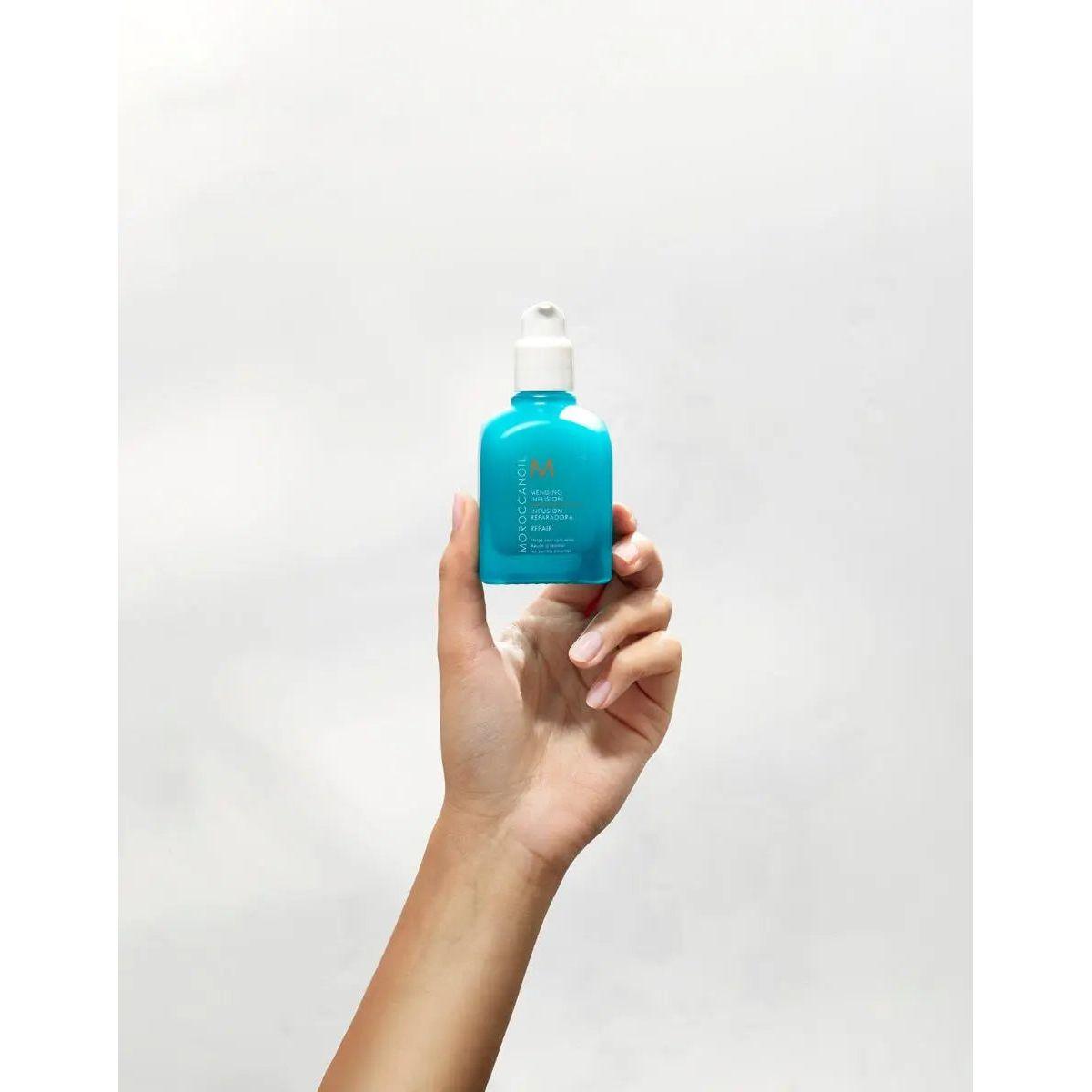 Hand holding Moroccanoil Repair Mending Infusion bottle for split ends and frizz control.