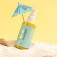 Alt Tag: Rio De Janeiro Dry Shimmering Oil with lime and coconut scent, yellow gold tint, 2 oz bottle on sandy beach with seashell.
