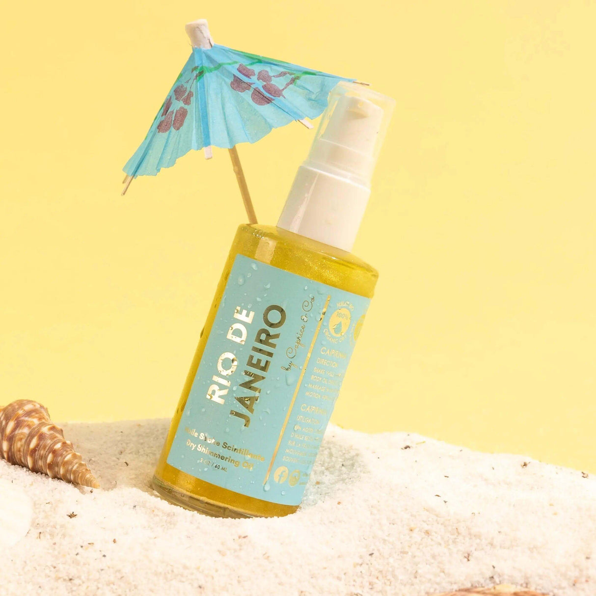 Alt Tag: Rio De Janeiro Dry Shimmering Oil with lime and coconut scent, yellow gold tint, 2 oz bottle on sandy beach with seashell.