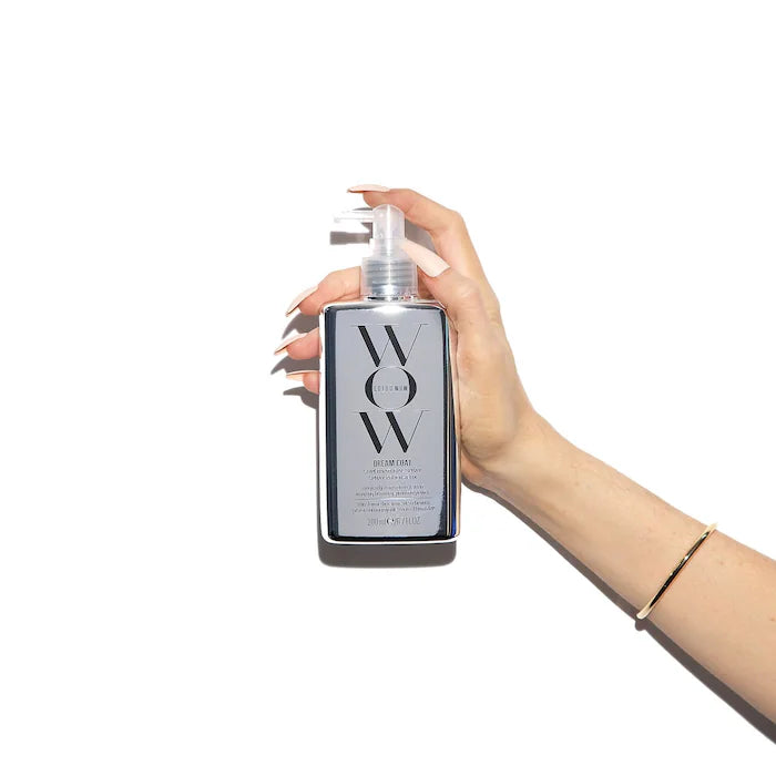 Hand holding Dream Coat Supernatural Spray Anti-Frizz Treatment bottle against white background