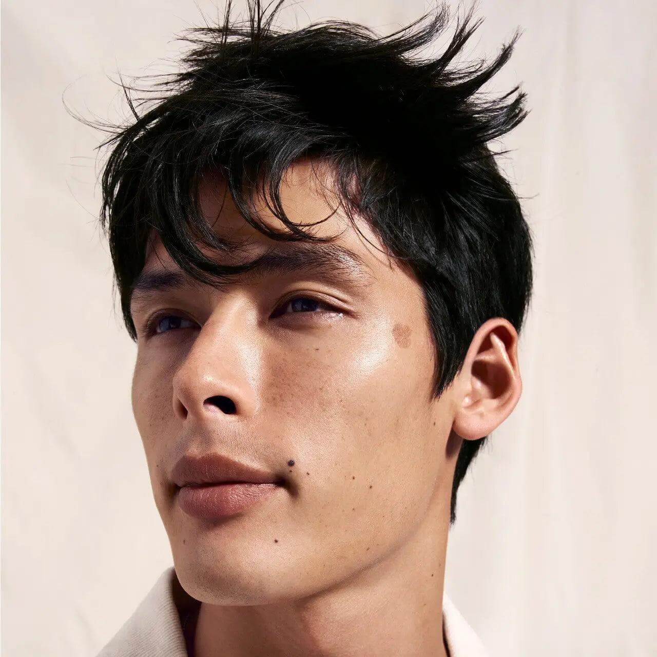 Portrait of a man with tousled black hair looking upward against a neutral background.