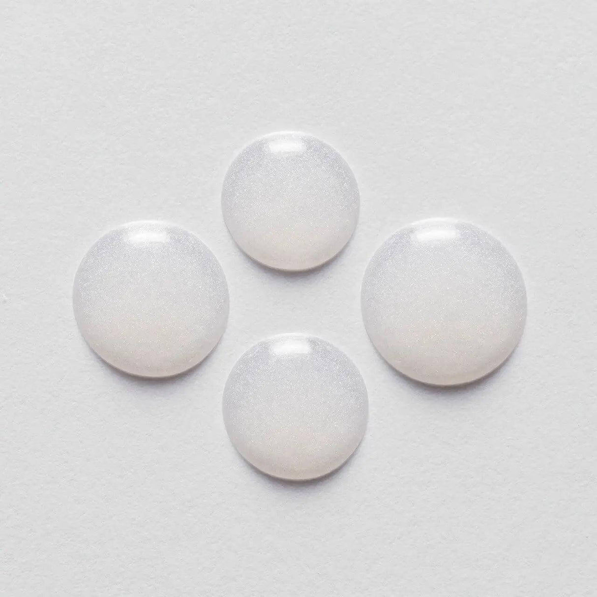 Four round drops of Kérastase Serum Extentioniste on a white background, showcasing its texture and consistency.