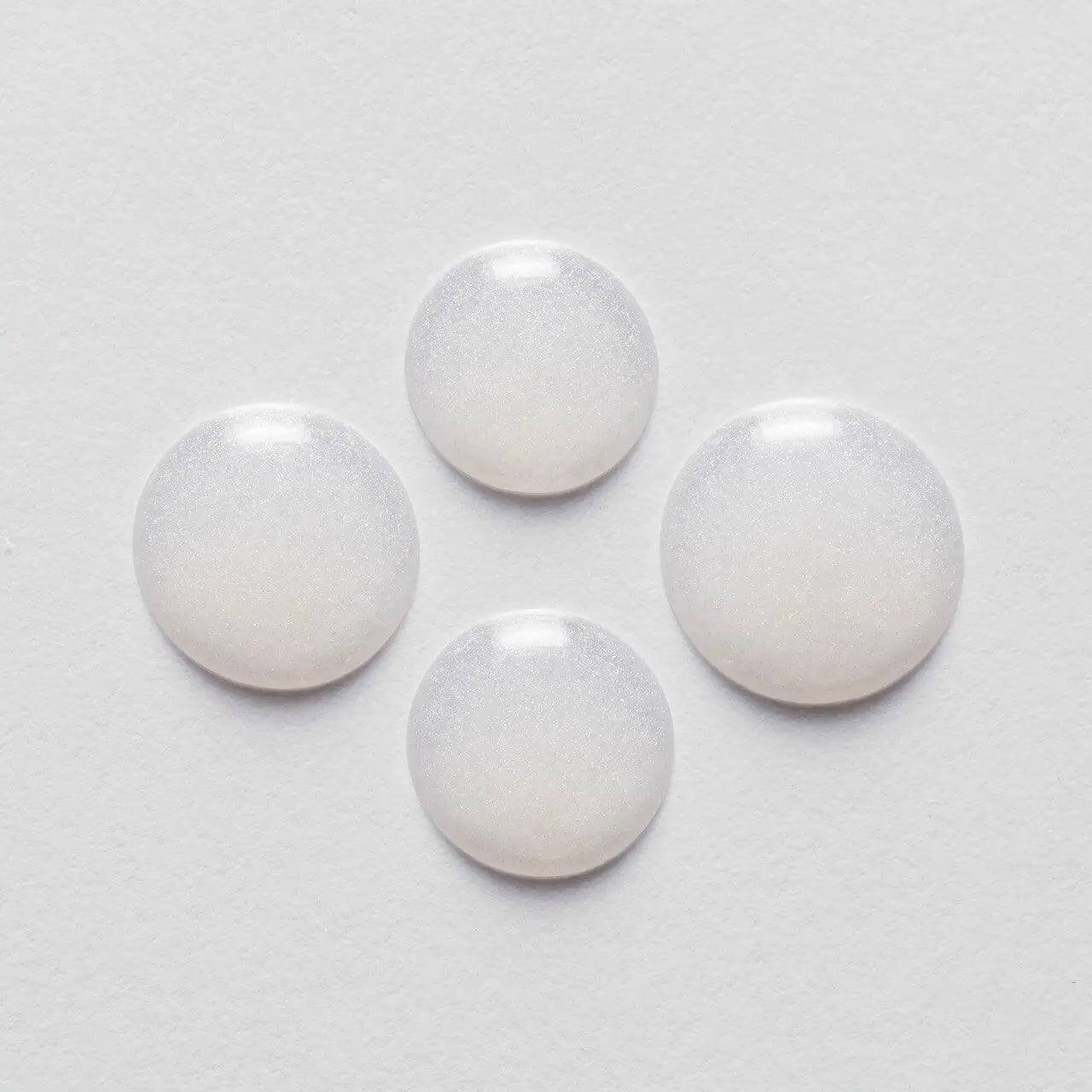 Four round drops of Kérastase Serum Extentioniste on a white background, showcasing its texture and consistency.