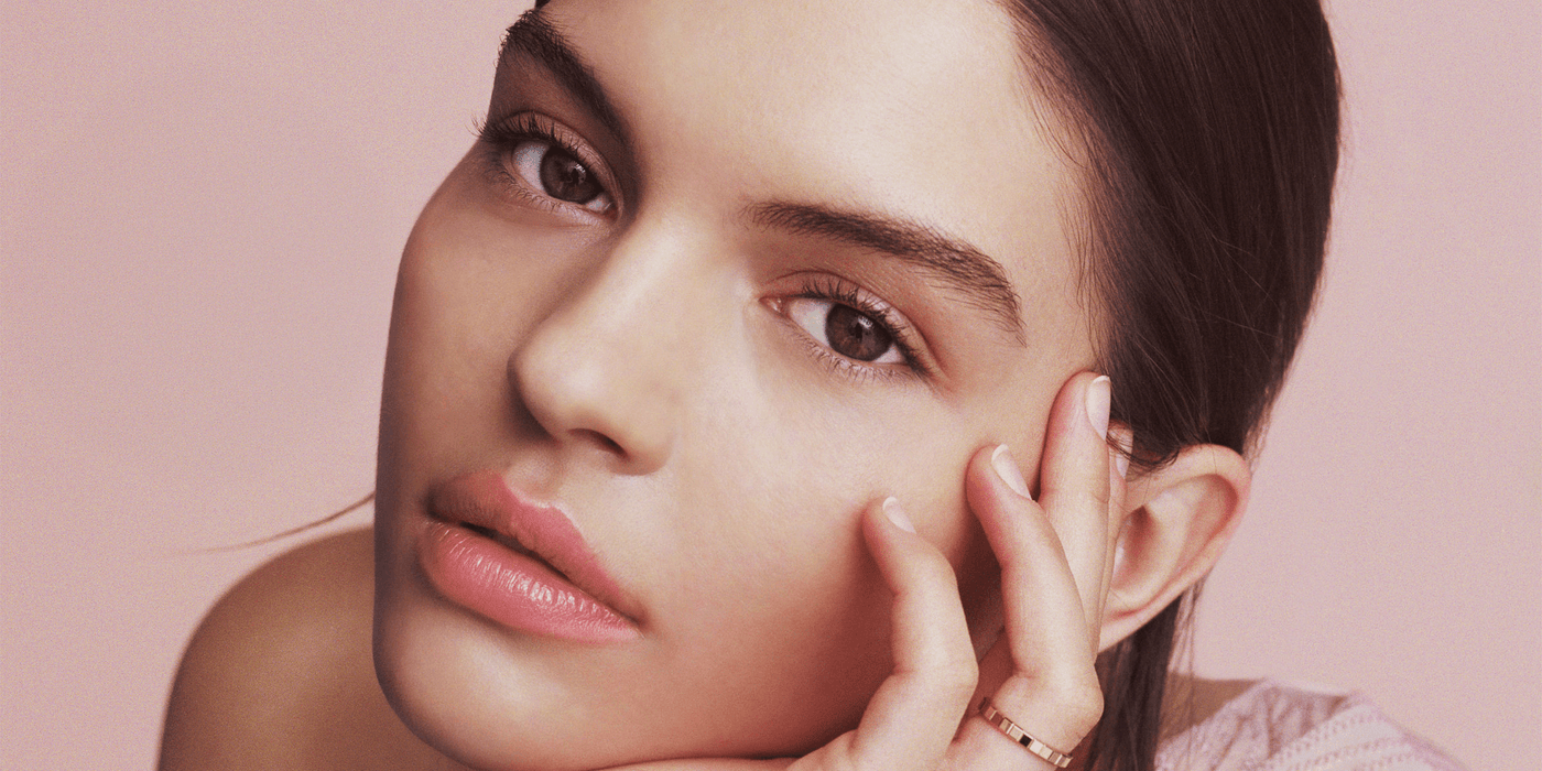 Close-up of a young woman with natural makeup and soft pink background, showcasing a minimalist beauty style.