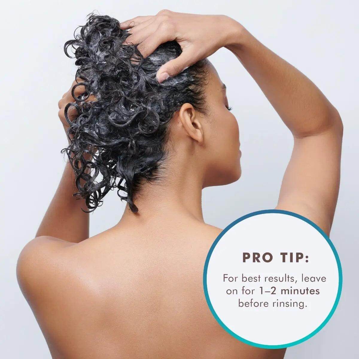 Woman applying Moroccanoil Smoothing Conditioner to curly hair with pro tip to leave on for 1-2 minutes before rinsing.
