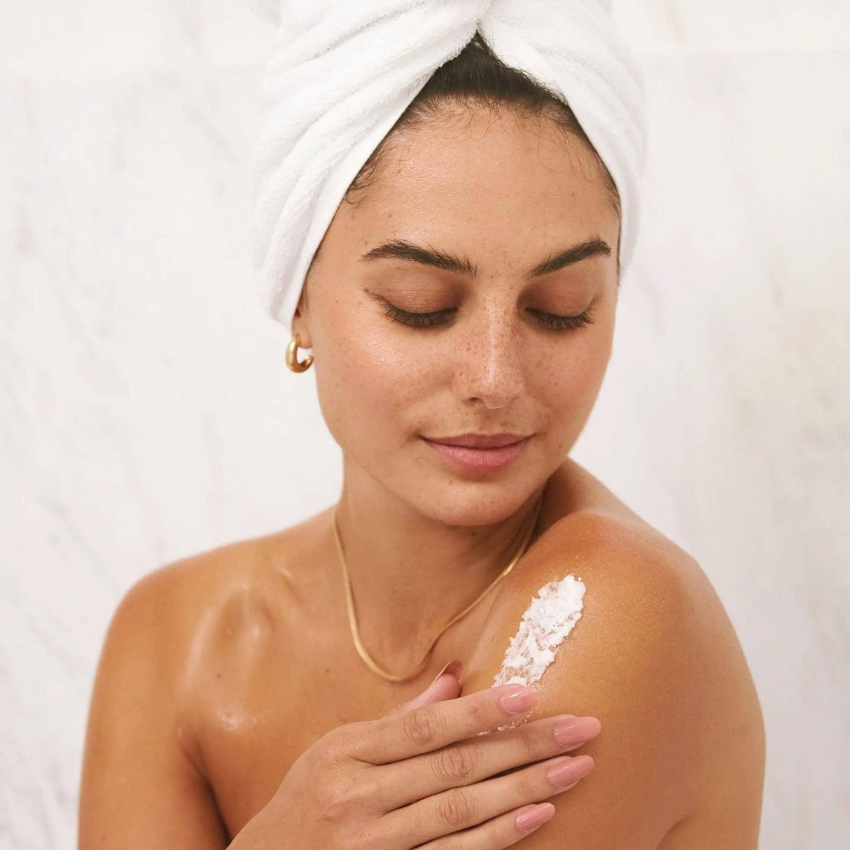 Woman applying Sugar Kiss Sugar Scrub on shoulder for exfoliation and hydration, emphasizing glowing skin and body care.