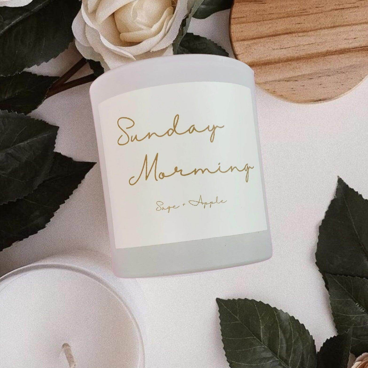 Alt Tag: Sage and apple scented candle "Sunday Morning" in elegant glass jar with wooden lid, surrounded by greenery and decor.