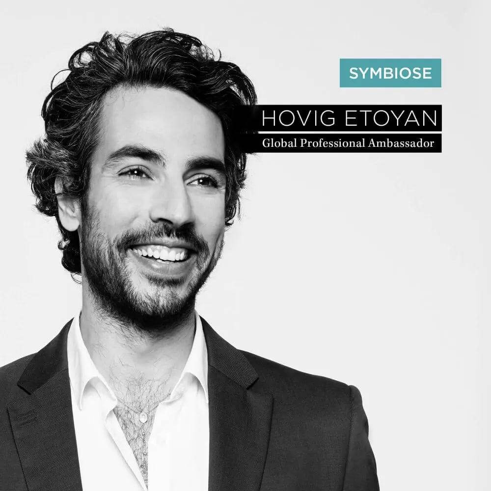 Smiling individual with dark curly hair in a suit, featuring Symbiose branding and ambassador recognition text.