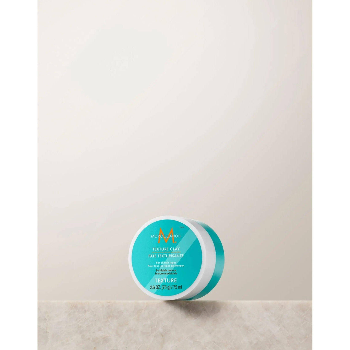 Moroccanoil Texture Clay jar on a neutral background, offering matte finish and strong hold for tousled, natural hairstyles.