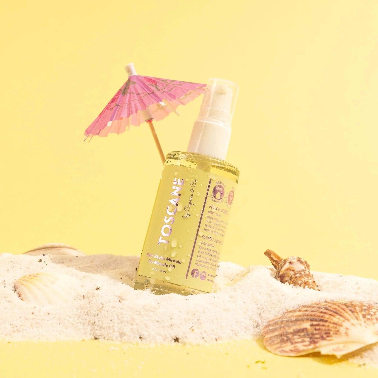 Toscane Dry Miracle Oil on sand with seashells and umbrella, peach sorbet scent, 2 oz bottle, organic illuminating body oil for skin glow