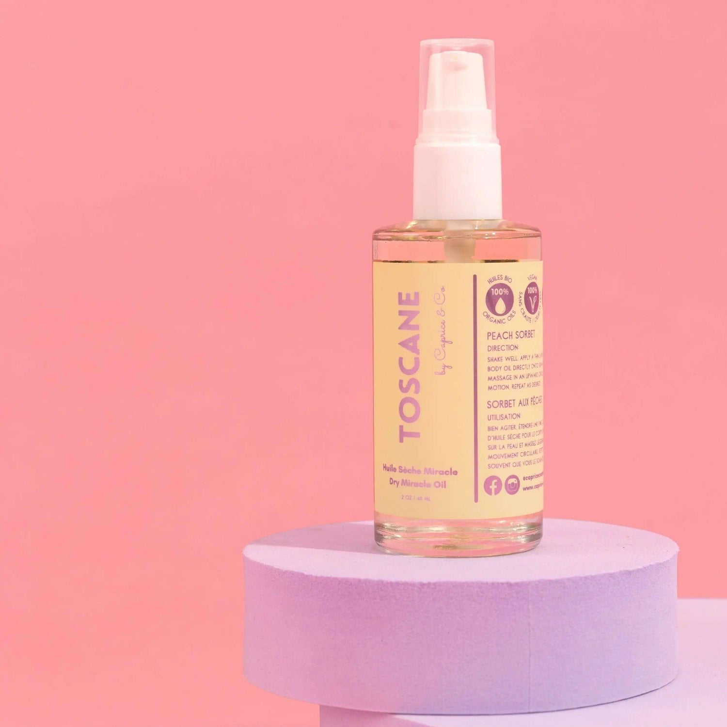 Toscane Dry Miracle Oil in 2 oz bottle with peach sorbet scent, placed on a pastel display against a pink background.