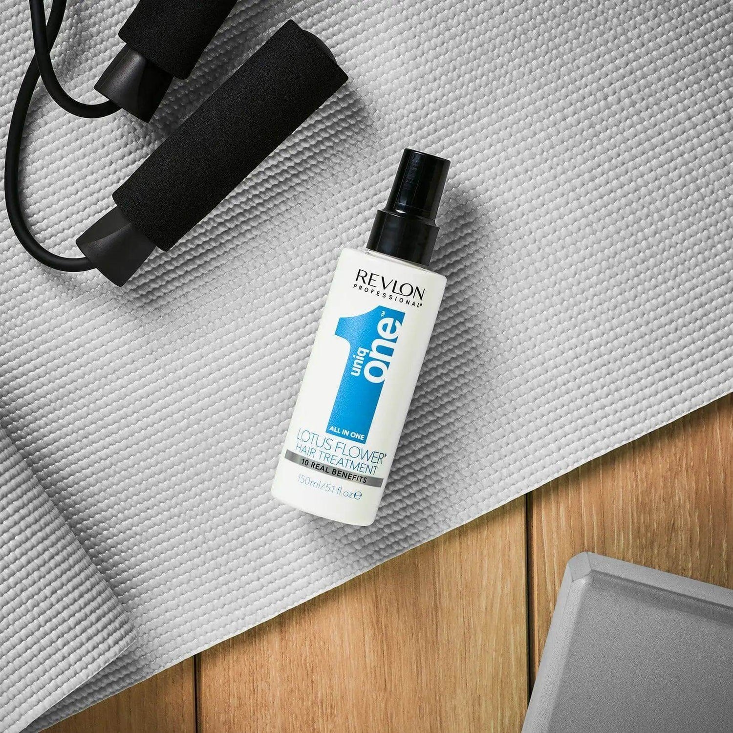 Uniqone ™ Lotus Flower Scent Hair Treatment bottle by Revlon on a wooden surface next to exercise equipment.