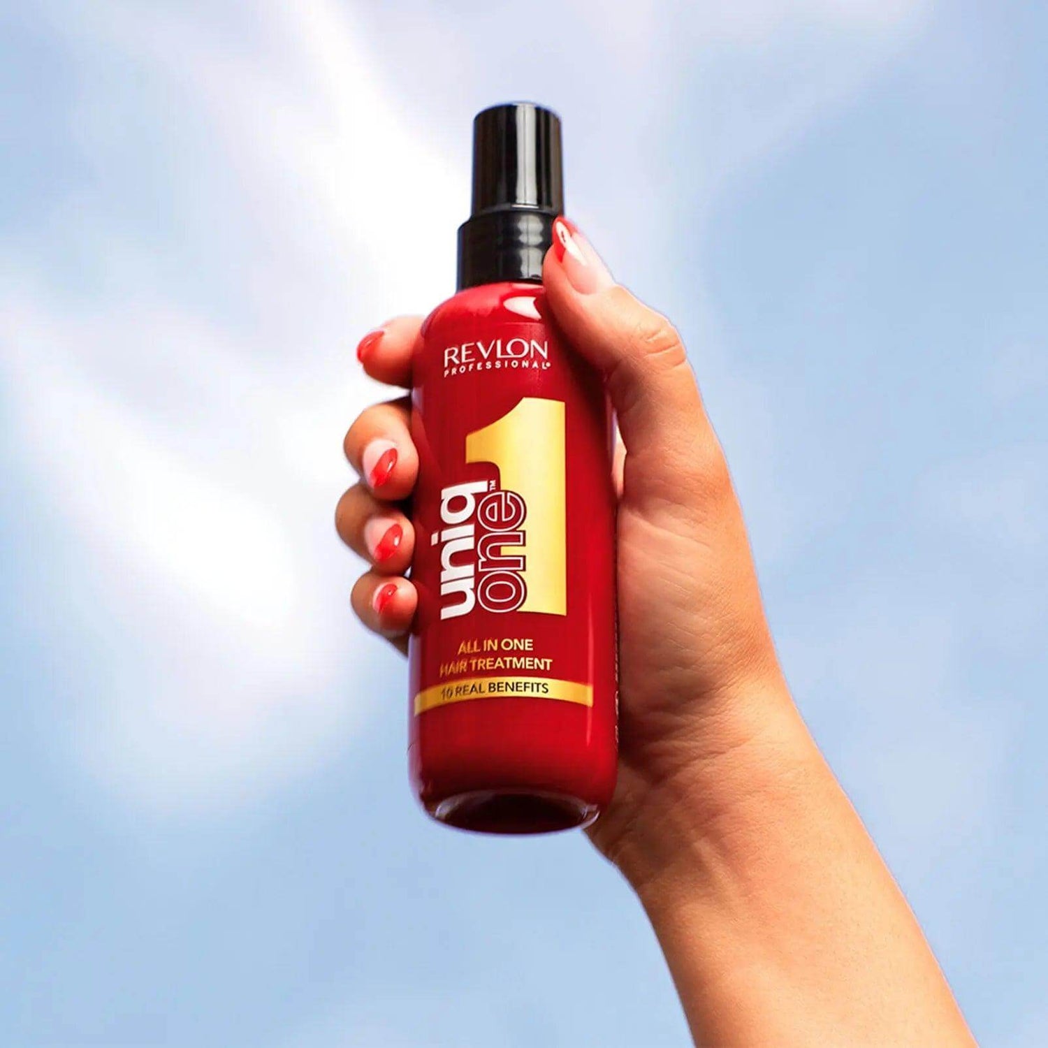 Hand holding Uniqone Hair Treatment bottle against blue sky, showcasing its all-in-one leave-in benefits for all hair types.