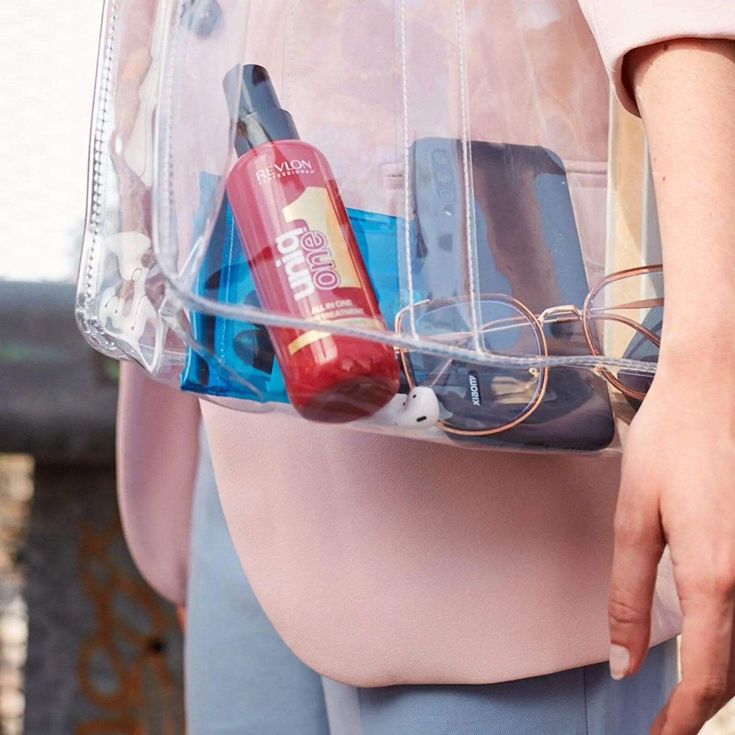 Clear bag containing Uniqone Hair Treatment bottle with sunglasses and phone.