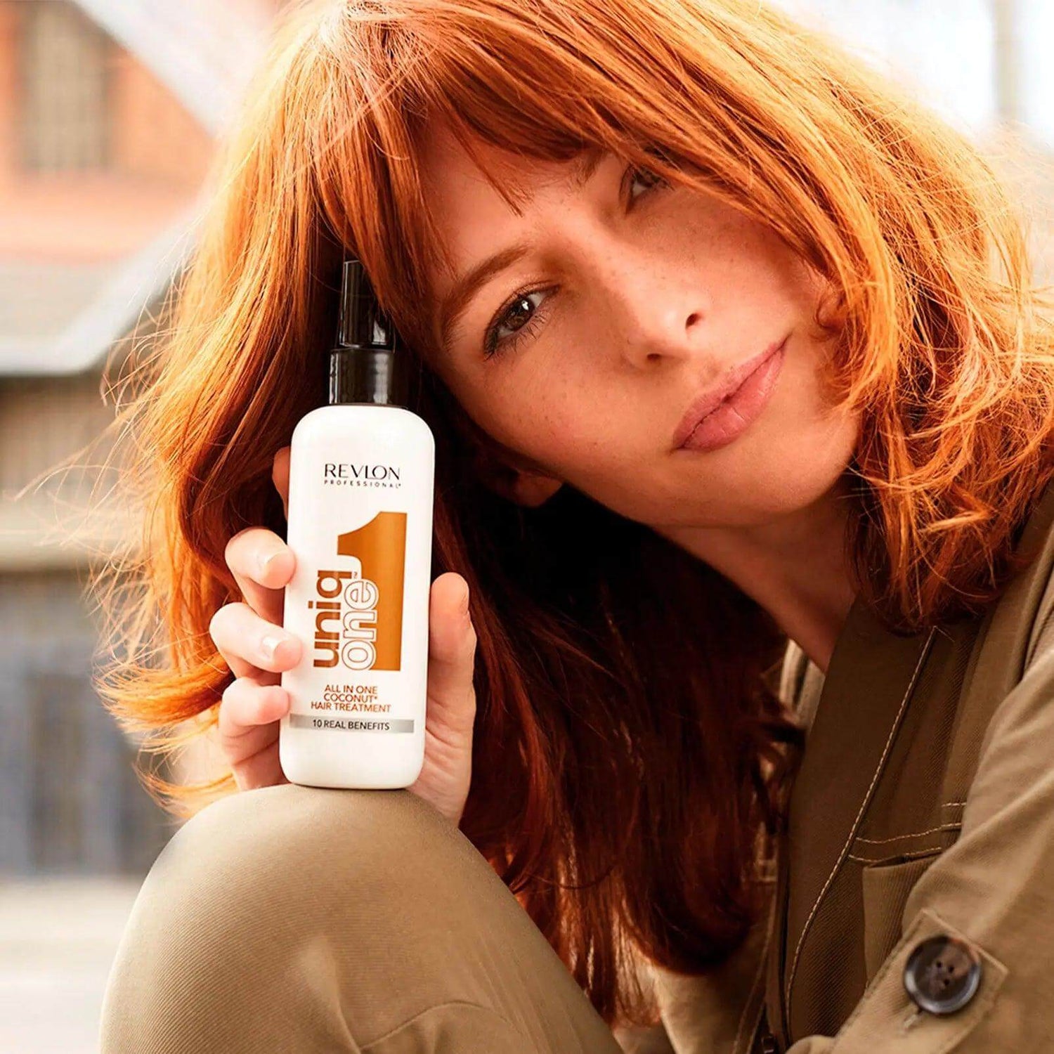 Woman showcasing Uniqone™ Hair Treatment Coconut Fragrance leave-in conditioner outdoors