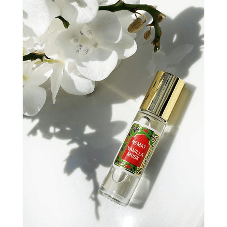 Vanilla roll-on perfume bottle with gold cap beside white flowers, close up.