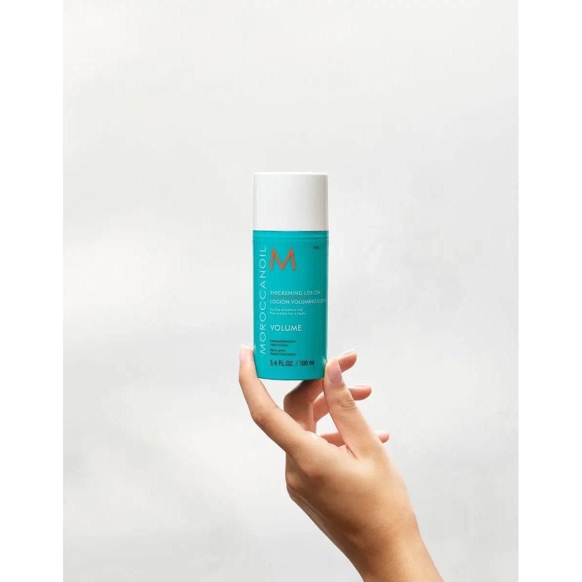 Hand holding Moroccanoil Volume Thickening Lotion bottle against a plain background.