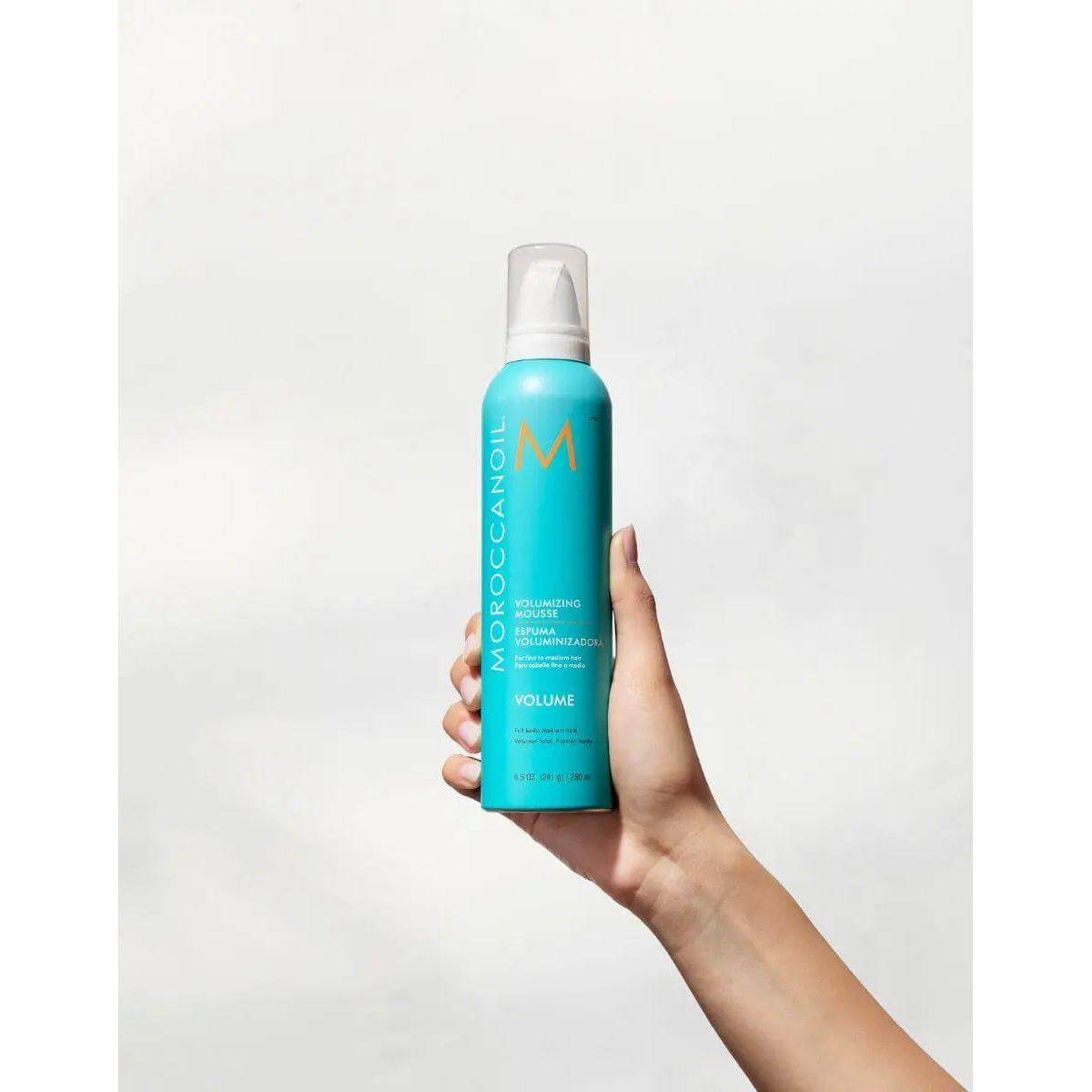 Hand holding Moroccanoil Volumizing Mousse bottle for instant hair volume and lift