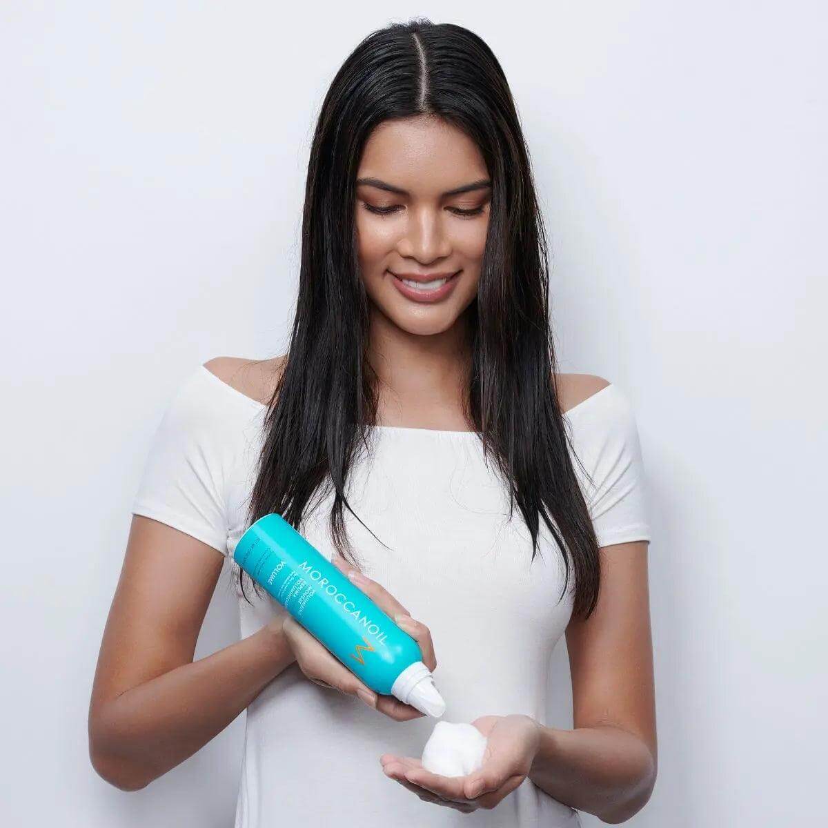 Woman applying Moroccanoil Volumizing Mousse to hand for hair styling and added volume.