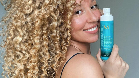 Woman showcasing a hair product with her curly hair visible.