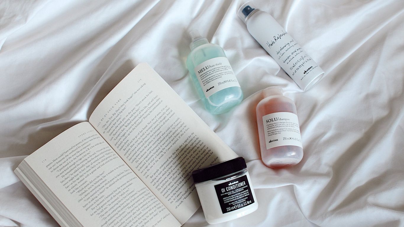 Skincare products and an open book on a white bedspread.