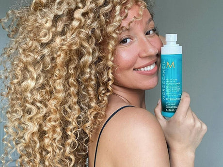 Woman showcasing a hair product with her curly hair visible.
