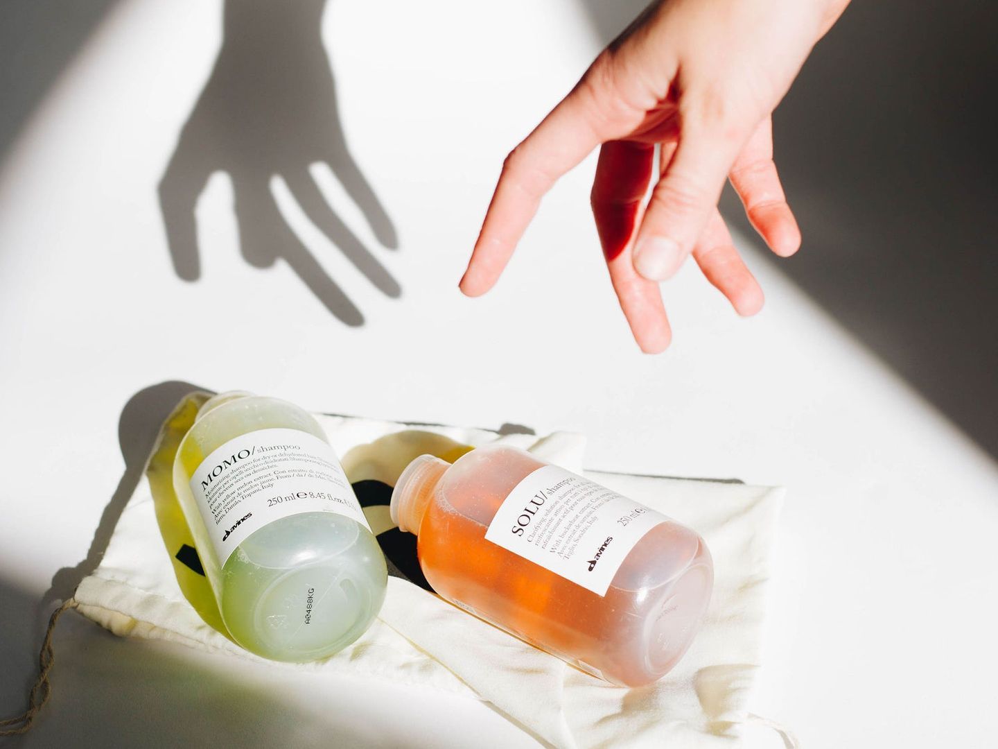 Hand reaching for skincare bottles casting shadow on surface.