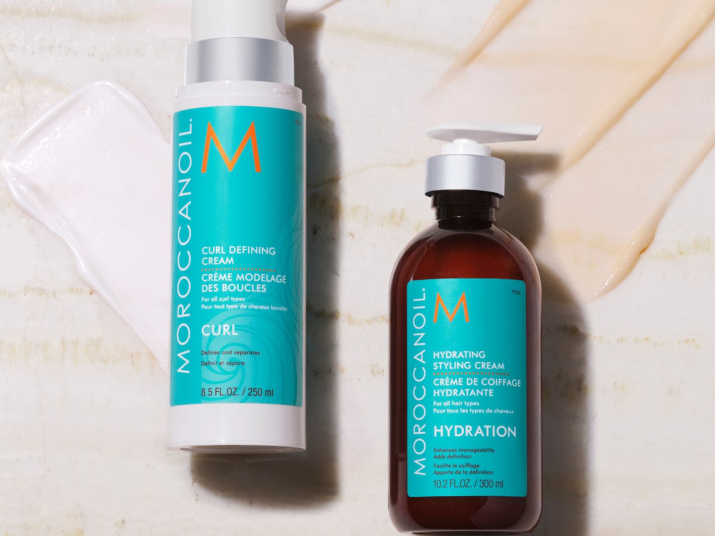 Two bottles of Moroccanoil hair products on a textured surface.