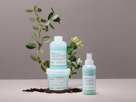 Bottles of haircare products with plants on a neutral background.
