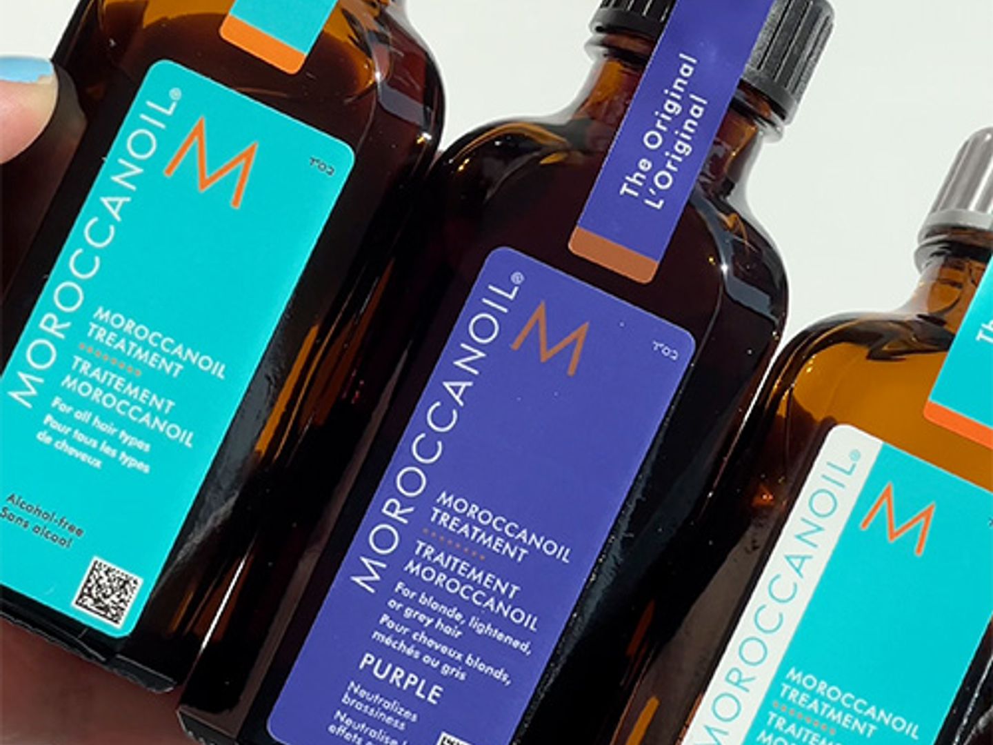 Three bottles of Moroccanoil hair treatment products held by a person.