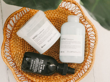 Hair care products arranged in a wicker basket with leaves.