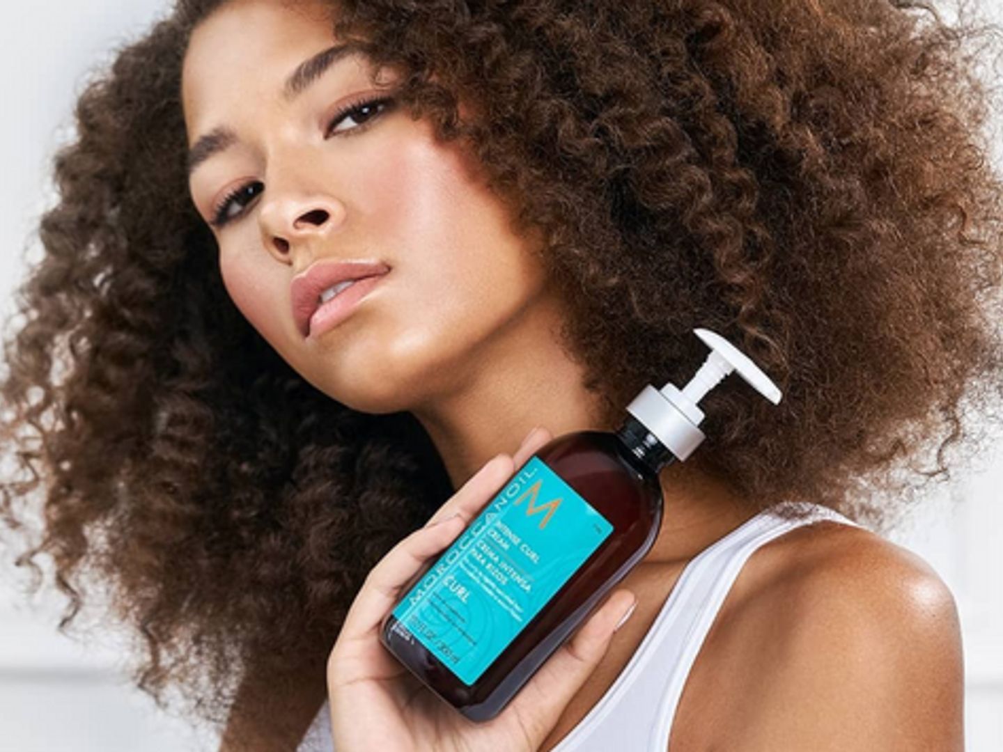 Person holding hair product bottle, showcasing healthy curly hair.