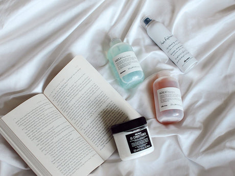 Skincare products and an open book on a white bedspread.