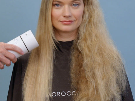 Person with half straight, half curly hair, holding a product.