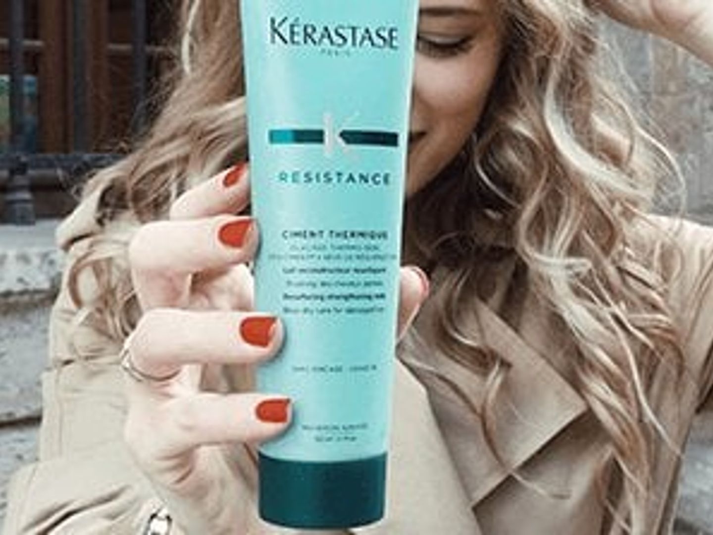 Person holding a Kerastase hair product with a subtle smile.
