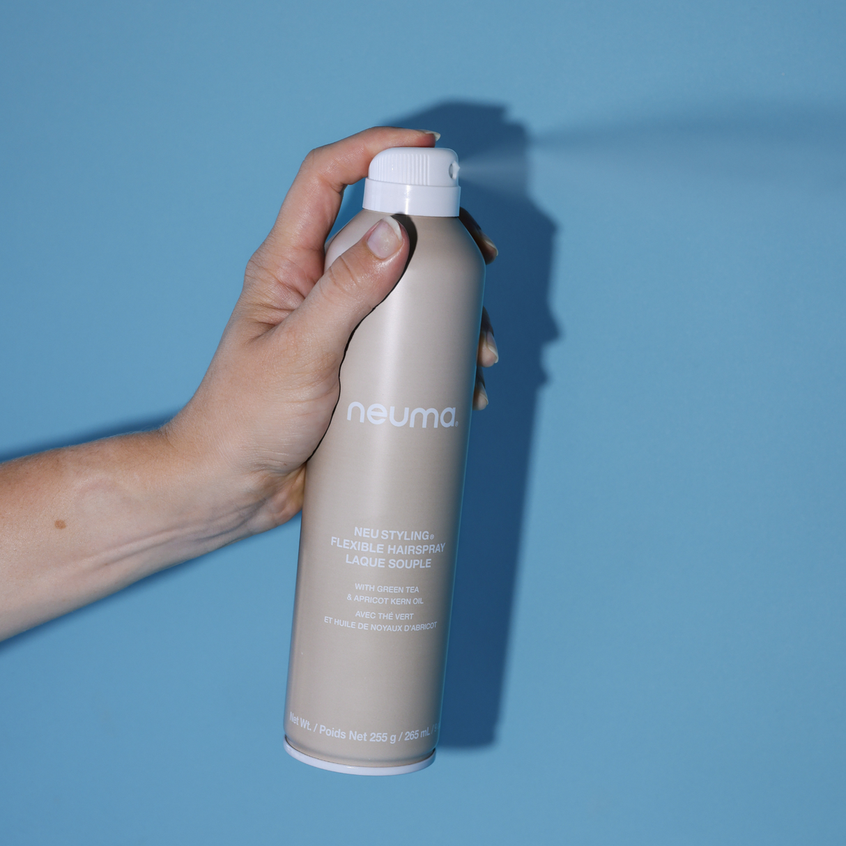 Hand holding Neu Styling Flexible Hairspray bottle against a blue background, offering medium hold and controlling humidity.