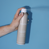 Hand holding Neu Styling Flexible Hairspray bottle against a blue background, offering medium hold and controlling humidity.