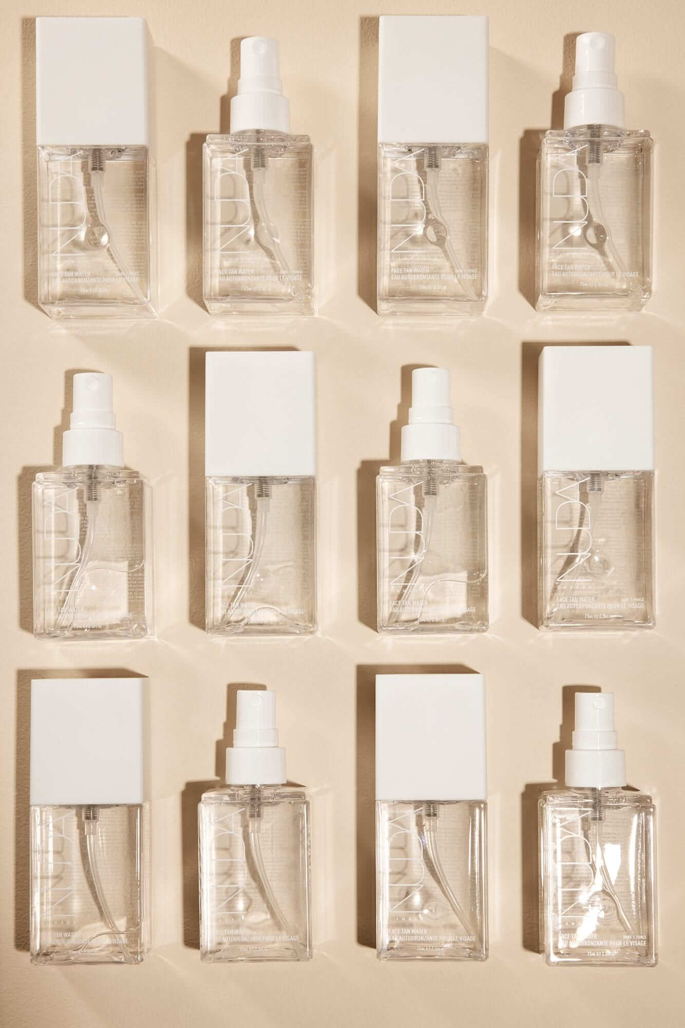 Empty clear bottles with white caps arranged in a grid pattern on a beige background.