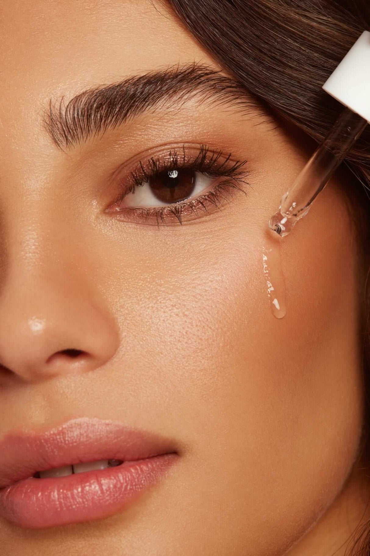 Close-up of a woman applying glowing serum from a dropper to her cheek for radiant skin.